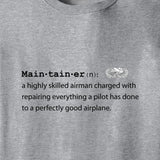 Close-up of a heather gray t-shirt featuring a black printed dictionary-style definition of 'Main·tain·er' with a small white airplane emblem.