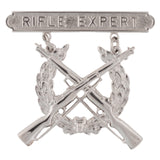 Silver 'Rifle Expert' badge with crossed rifles and laurel wreath on a white background