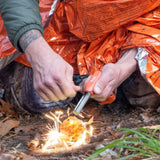 Person using a fire starter tool to ignite a fire with orange insulation material in the background.