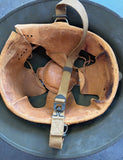 A vintage military-style helmet with a heavily worn tan leather interior lining and tan chin strap, resting inside a dark olive green metal helmet shell.