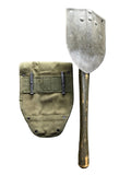 A vintage military-style shovel with a weathered dark metal blade and a khaki canvas sheath featuring a flap, pocket, and a small tan leather patch, shown against a plain white background.