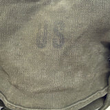 Close-up of a canvas bag or pouch in olive drab green, showing a faded dark 'US' marking on the front.