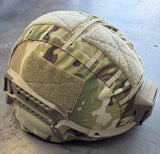 A tactical helmet cover in a multi-terrain camouflage pattern with beige fleece panels, shown fitted on a helmet against a concrete floor.