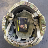 Top-down view of a military tactical helmet in Multicam camouflage pattern, showing the interior padding, straps, and a packaged insert card.