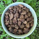 Brown bark or wood chips in a white plastic tub placed outdoors on green grass and leaves.