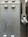 Close-up of a dark gray metal mechanical component with a stamped logo and a small silver metal pin or roller on the right side.