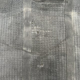 A close-up of a black textured fabric with a grid-like woven pattern and a vertical seam down the center.