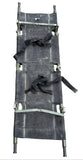 A used military-style stretcher or cot with a dark gray canvas body, olive green metal frame, and black straps, photographed on a gray concrete surface.