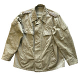 A military-style field jacket with a vertical textured stripe pattern in olive green and tan, laid flat on a gray concrete surface.