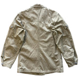 A light beige corduroy utility jacket shown from the back, laid flat on a textured gray concrete floor.