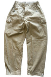 A pair of light olive green and beige vertically striped cargo pants laid flat on a gray concrete floor.