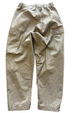 A pair of beige and brown vertically striped cargo pants laid flat on a gray concrete floor.