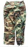 A pair of vintage woodland camouflage cargo pants laid flat on a gray concrete surface. The camouflage pattern features green, brown, tan, and black shapes.