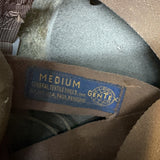 Close-up of a brown woven textile label inside a garment, showing the text 'MEDIUM' and 'GENTEX' on a blue patch.