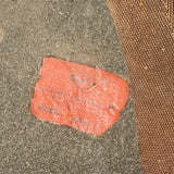 A close-up of a textured orange-red rubber patch or seal attached to a gray concrete-like surface, with a brown woven fabric or mat visible along the right side.