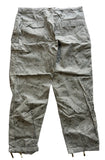 A pair of olive green cargo pants with a small white geometric pattern, laid flat on a gray concrete floor.