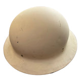 A vintage cream-colored military combat helmet with a wide brim, resting on a dark gray concrete floor.