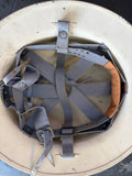 An interior view of a light beige hard hat showing the gray adjustable chin strap, ventilation holes, and tan foam padding.
