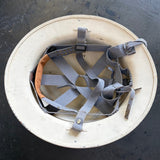 An off-white hard hat viewed from above, showing the interior with gray adjustable straps and a small orange lining.