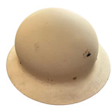 A vintage cream-colored hard hat with a wide brim, resting on a dark gray concrete floor. The hard hat shows some scuffs, dirt, and minor damage, including a small dark spot on the right side.