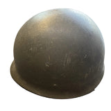 A vintage olive drab military helmet resting on a concrete floor.
