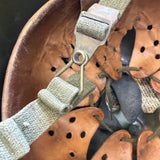 Close-up of a brown leather helmet with adjustable fabric straps and metal buckle hardware.