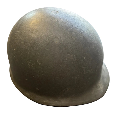 A vintage olive drab military helmet, likely a World War II M19 style helmet, resting on a concrete floor.
