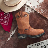 A tan leather western boot with decorative cutouts and a rugged dark sole, styled on a brown and white cowhide rug with a cream cowboy hat, red bandana, and a Texas license plate visible.